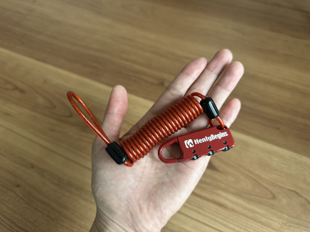 手のひらに載せたデイトナのワイヤーロックDLK120（カールコードとダイヤル錠のサイズ感）